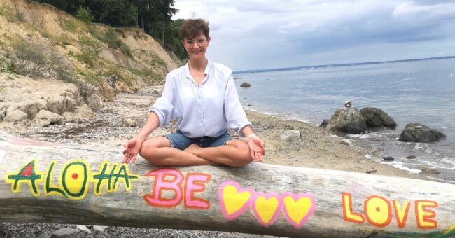 Fun Facts über Simone Simone sitzt auf einem ausgewaschenen und bemalten Baumstamm am Meer.