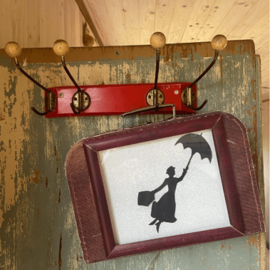 Ein kleiner Koffer hängt an einer Garderobe, Sinnbild für "den Alltag an der Garderobe abgeben"